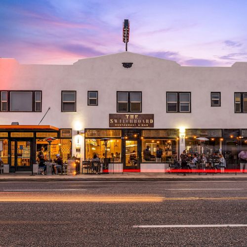 A street view of a two-story building with multiple businesses, including a restaurant with outdoor seating and a 